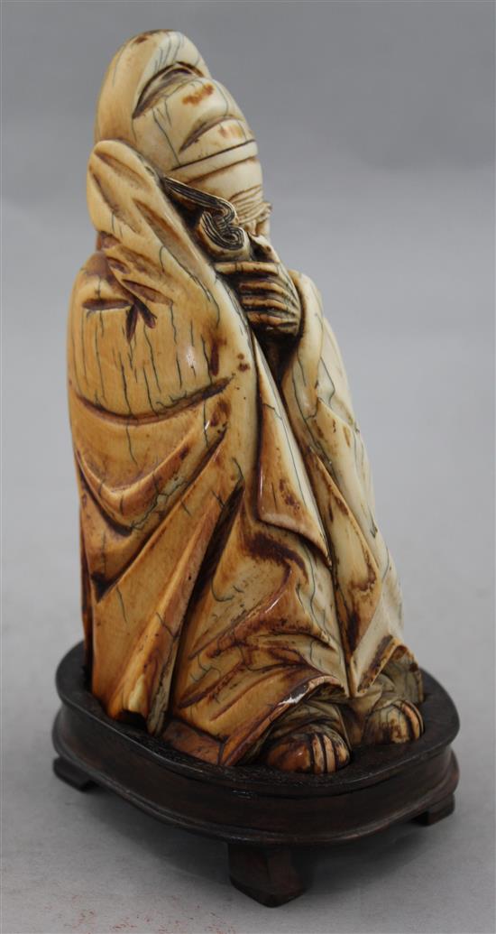 A Chinese mammoth ivory carving of a seated figure of Li Bai, holding a book, 16.5cm, wood stand